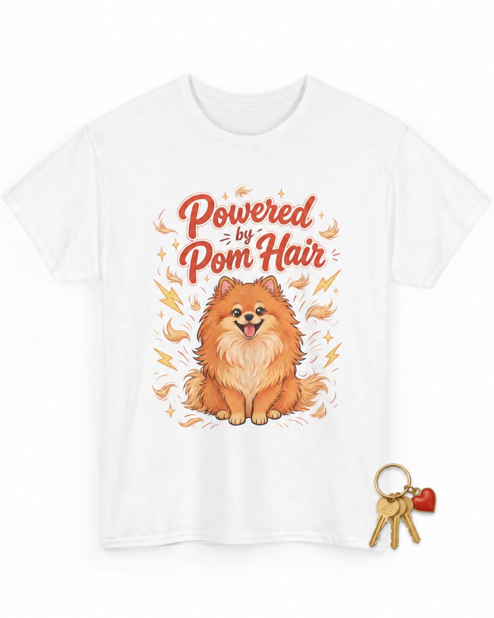 Powered by Pom Hair T-shirt flat lay featuring a white tee with a cheerful orange Pomeranian, gold keys, and a red heart keychain